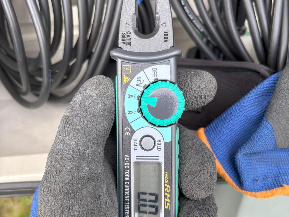 手袋をした手で、電流を測る測定器をケーブルに当てているところ
